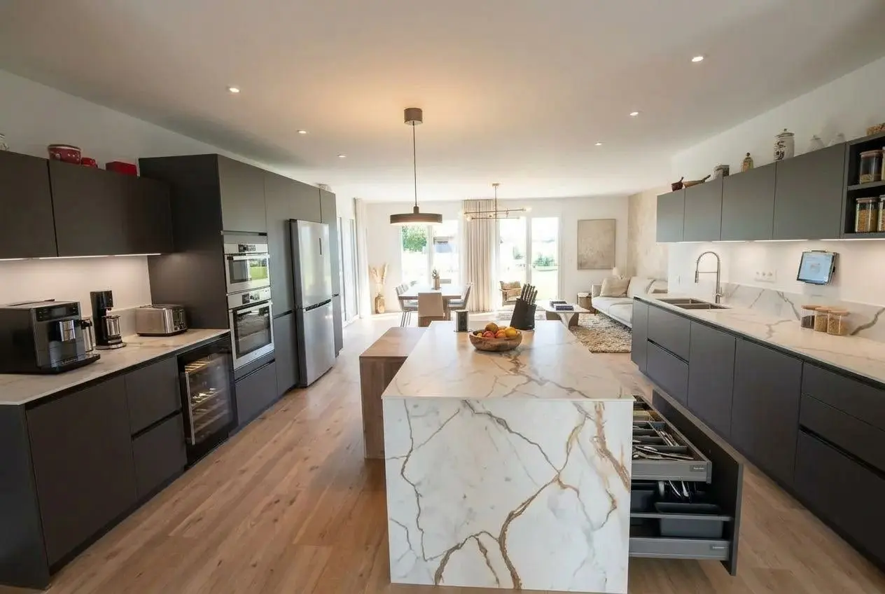 Cuisine ouverte sur salon moderne avec îlot central en marbre et rangements gris foncé, espace lumineux et fonctionnel.